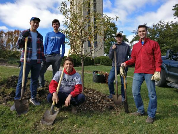 5 male student volunteers with shovels with planted tree by Campanile